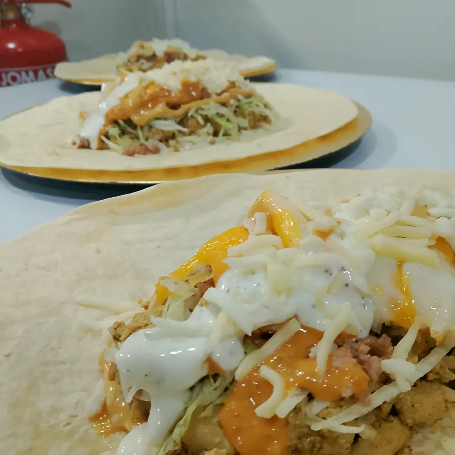 Un french tacos abierto mientras se prepara, con salsas y queso